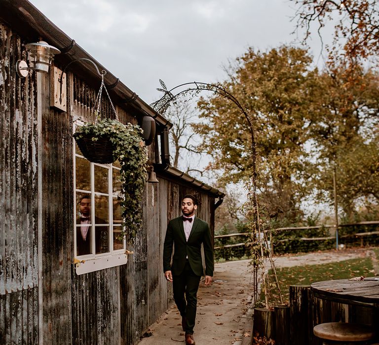 Groom in classic black suit with burgundy bowtie walking through Oak Tree Barn wedding venue 