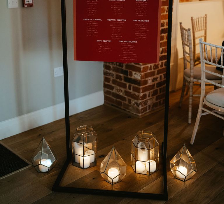 Orange & red wedding stationery with retro feel beside industrial styled lanterns with white pillar candles