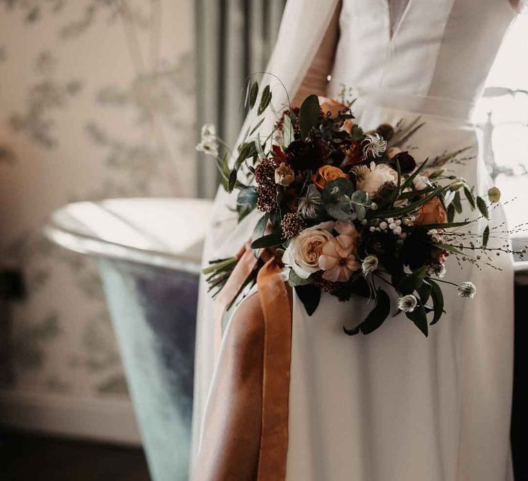 Bride in ivory wedding dress with front leg slit holding mixed neutral bouquet, wearing strapless wedding high heels with large white bow 