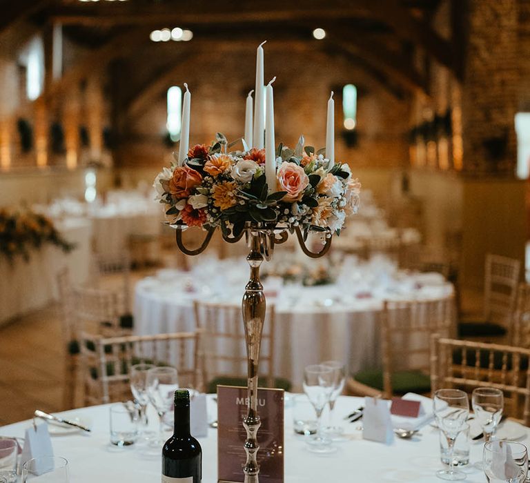 Peach, orange, and white wedding flowers on a gold candelabra with white candles for a tall statement table centrepiece idea 