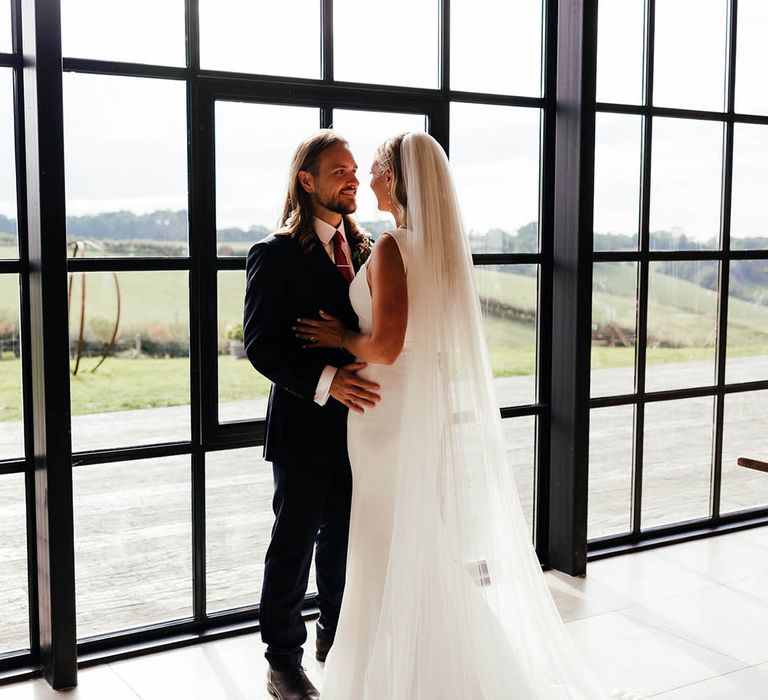 Bride and groom pose in front of the iconic windows at Botley Hill Barn in Surrey 