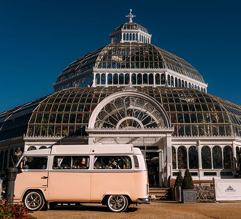 Pale pink VW camper van wedding transport in front of the incredible glass house wedding venue, Sefton Park Palm House 