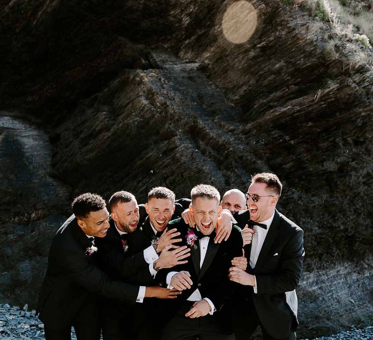 Grooms party wearing matching classic black-tie tuxedos, bow ties and grooms sunglasses on tunnels beaches 