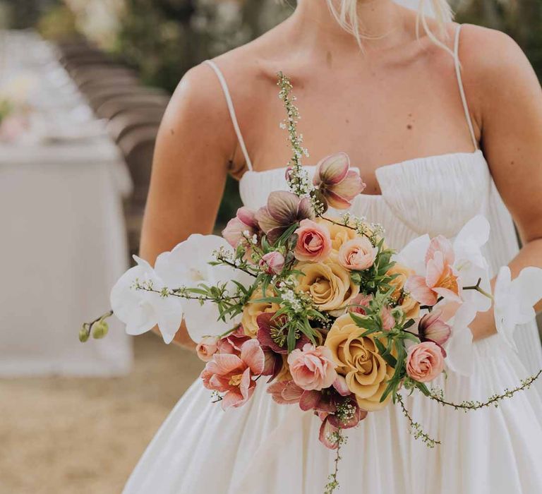 Bride in Watters strappy sleeveless princess wedding dress and chapel length wedding veil holding blush toned bridal bouquet with roses poppies peonies and foliage at Euridge Manor 