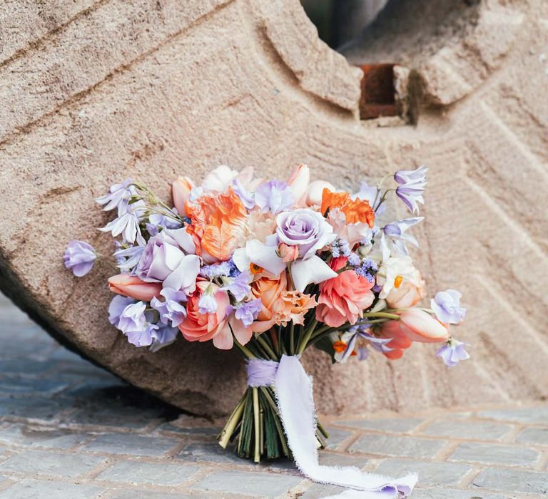 Bridal bouquet with peach garden roses, white peonies, lilac sweet peas, bluebells and wildflowers tied with lilac ribbon