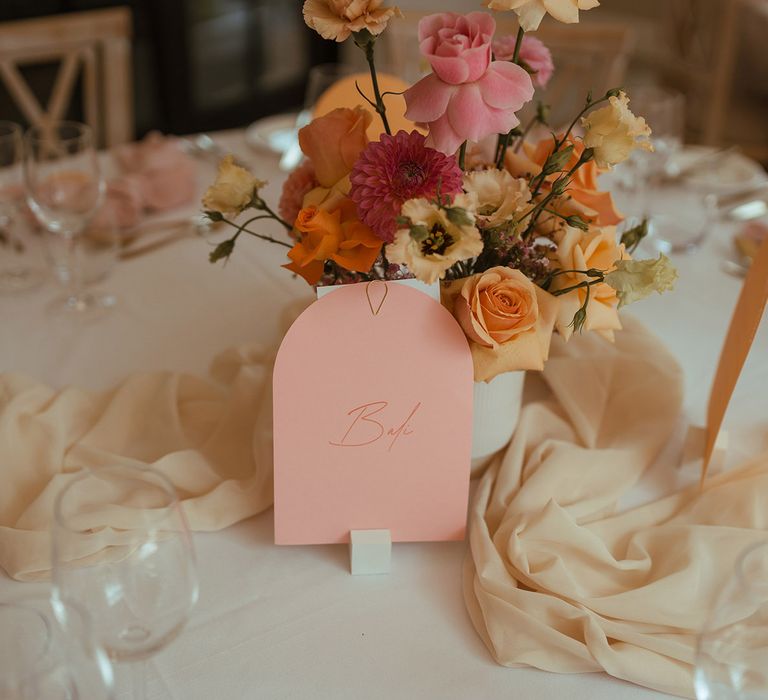 pink and yellow centrepiece flowers and arched wedding table sign 