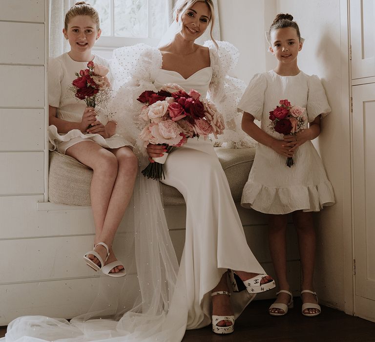 Bride sits with two flower girls in white dresses on a window seat at contemporary wedding at Middleton Lodge 