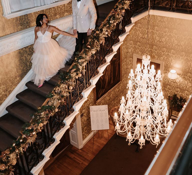 Groom in beige suit with bride in neutral reception ruffle dress walking down the stairs at luxe wedding venue 