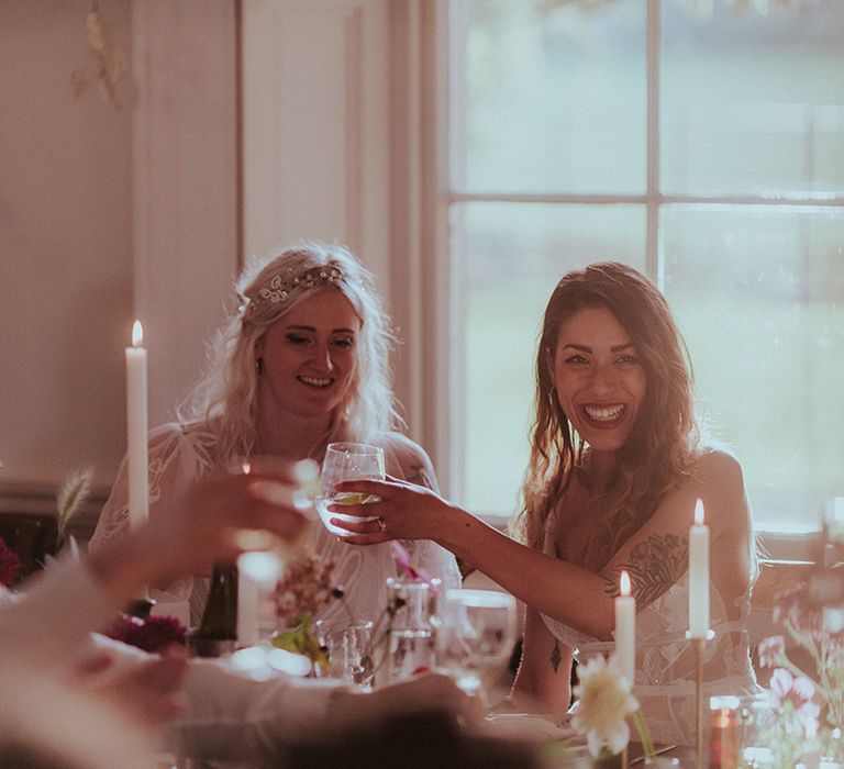 The two brides sit at their wedding breakfast and cheers their glasses at LGBTQI+ wedding 