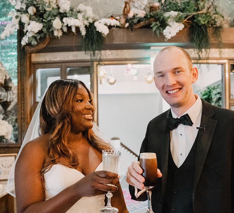 Bride in fitted mermaid wedding dress with groom in black tuxedo having celebratory drink after wedding ceremony 