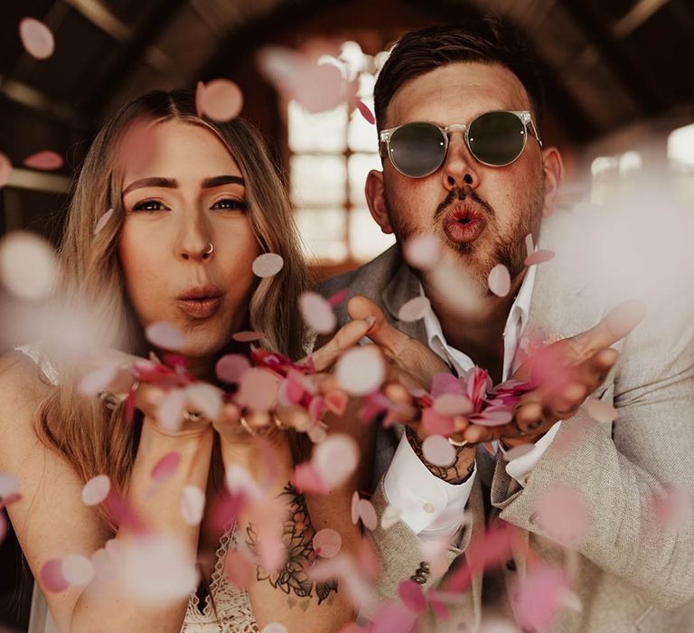 The bride and groom blowing pink, white and red confetti at their wedding in Wales 