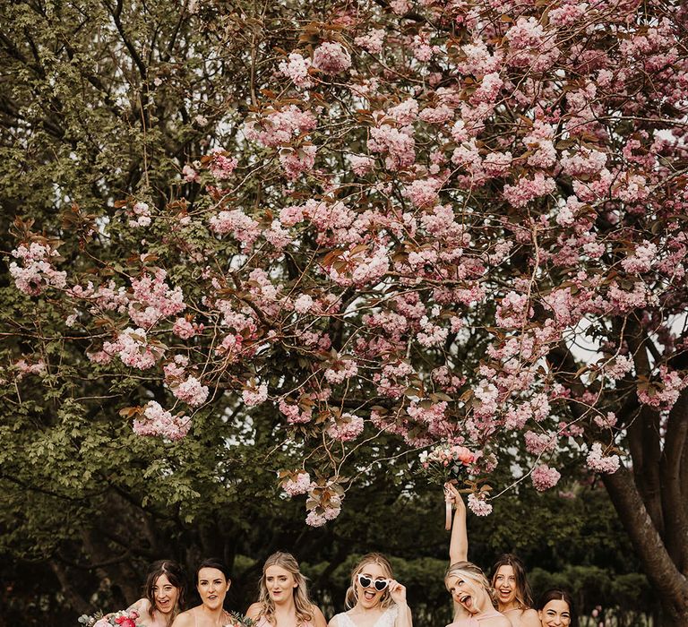 Bridal party wearing pink bridesmaid dresses with white heart shaped retro wedding sunglasses 