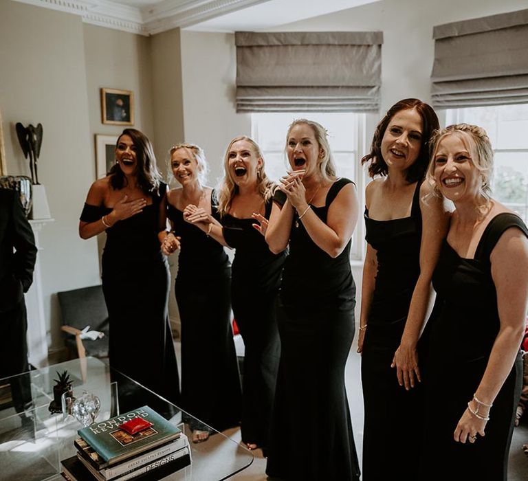 Bridal party wearing black bridesmaid dresses and react as they see the bride for the first time 