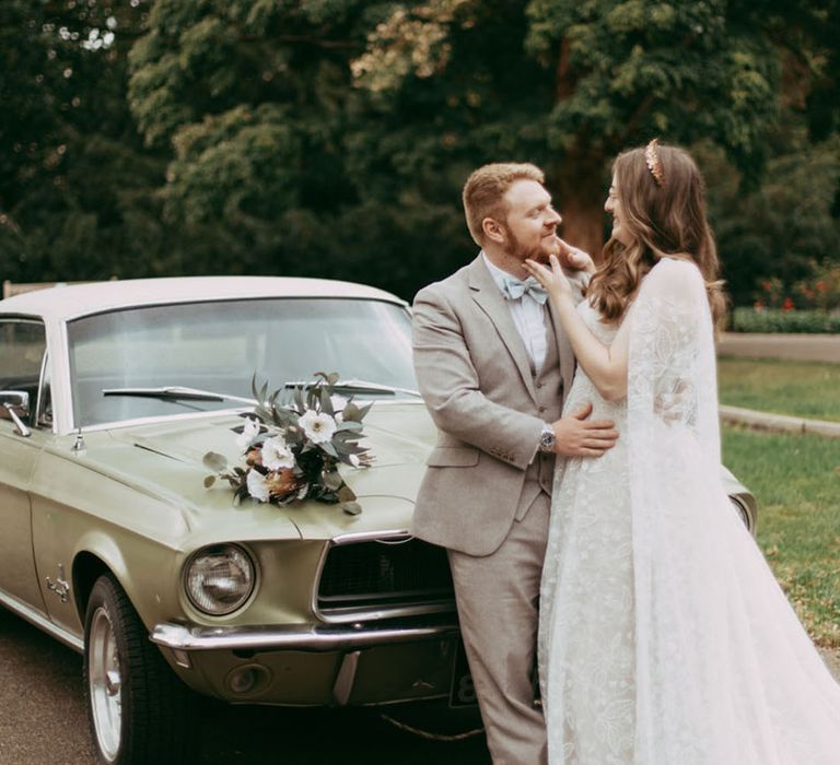 Classic green Mustang wedding car with the bride and groom leaning on the bonnet 