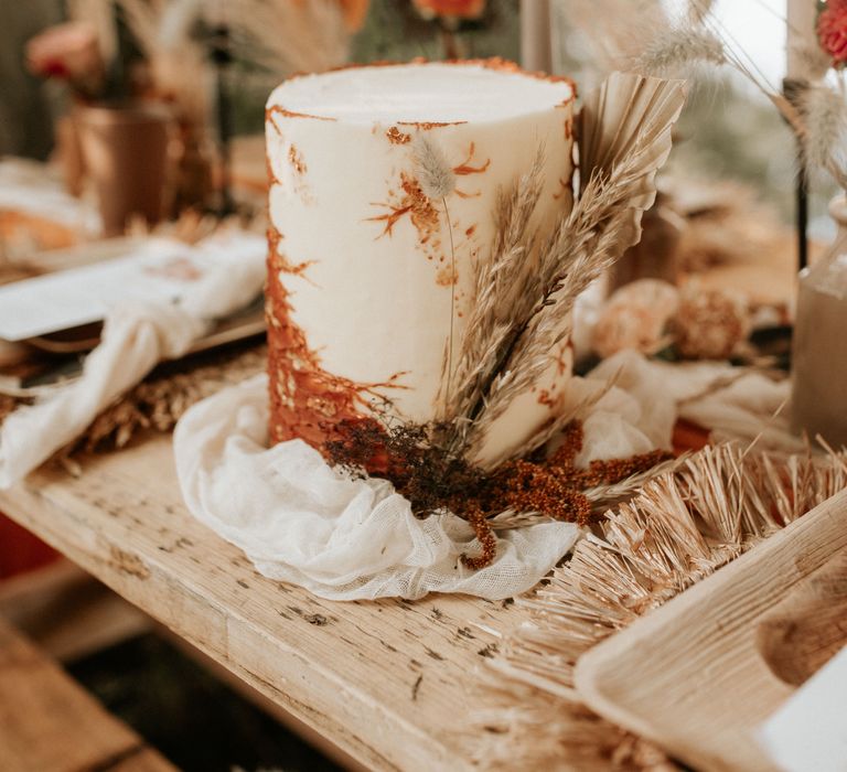 White and burnt orange wedding cake with gold leaf decoration on wooden table