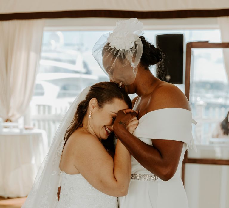 Black bride in blush veil with flower detail kissing her brides head on the dance floor 