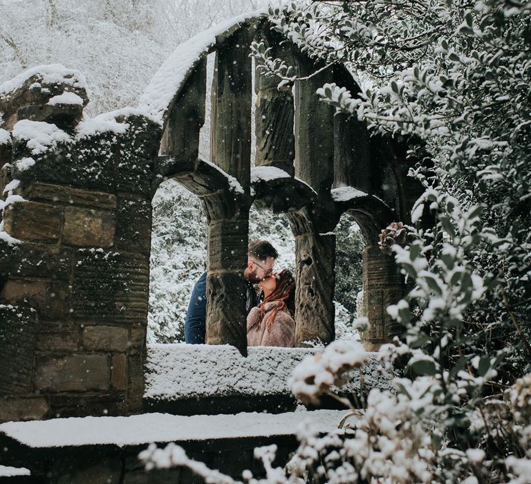 Bride and groom kiss in the snow through a stone archway at Cannon Hall