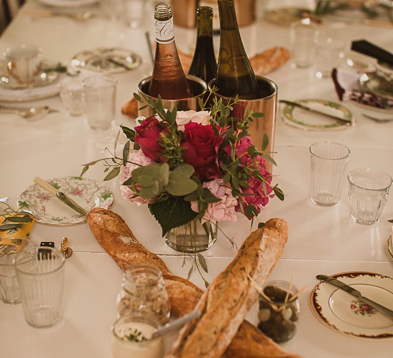 A wedding breakfast set up with two long french baguettes crossing each other and wine in a wine cooler. Photography by The Springles.