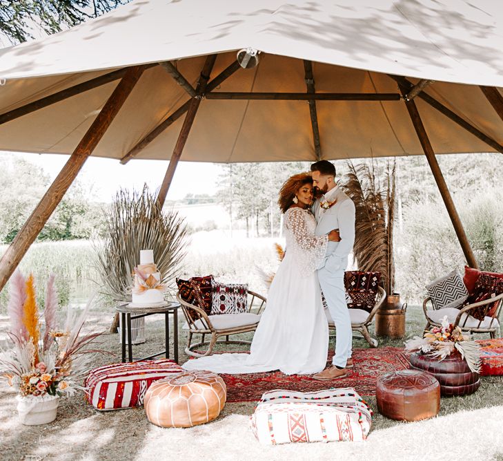 Bride & groom embrace outdoors underneath tipi 