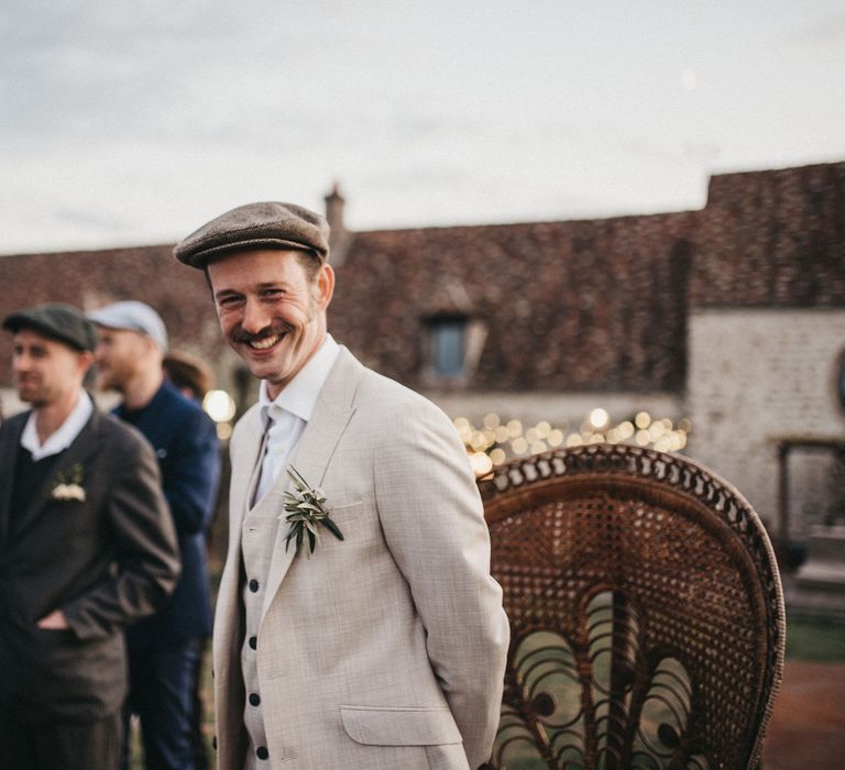 Smiley groom with moustache in a beige Peaky Blinders wedding suit and flat cap