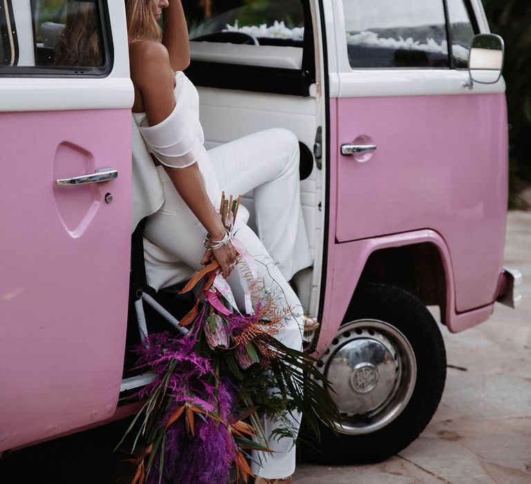 A bride sits in a pink VW Campervan with bouquet held loosely at her side. Photography by Stephanie Shenton.