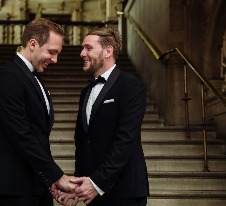 Grooms stand on staircase and hold hands