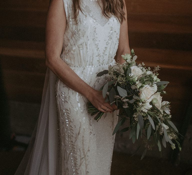 Bride holds white floral bouquet with green foliage