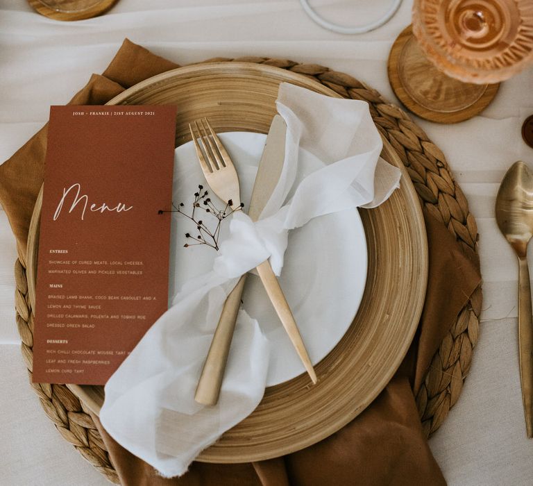 Neutral and terracotta wedding tablescape with gold cutlery, wooden and rattan details