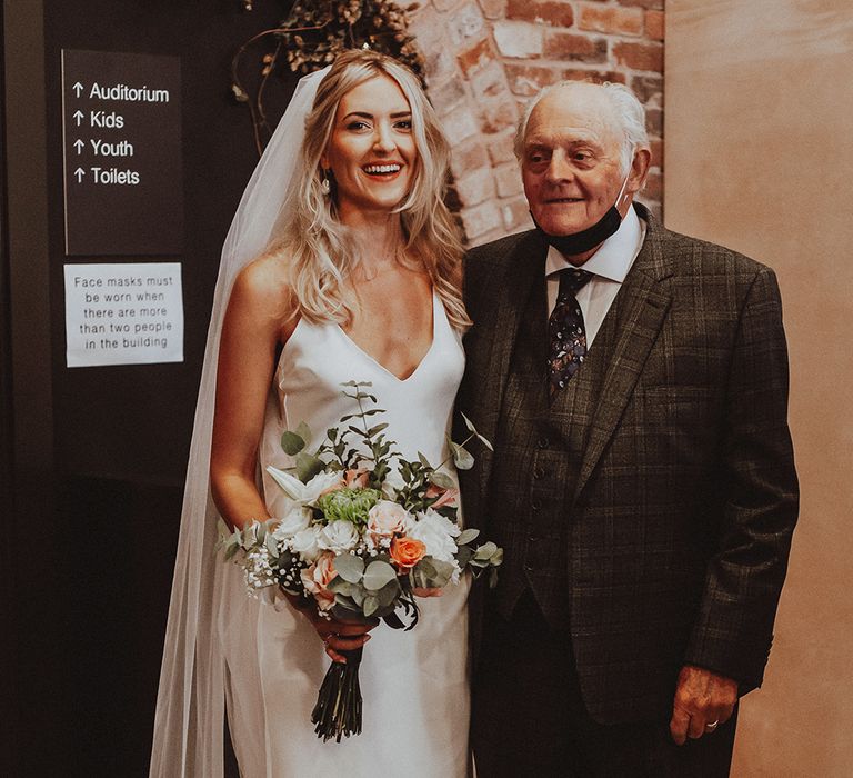 Bride in a fitted wedding dress and long veil with her grandad in a check suit 