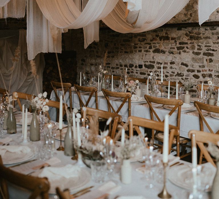 Exposed brick wedding venue, with wooden chairs, fabric ceiling, neutral flowers and taper candles 