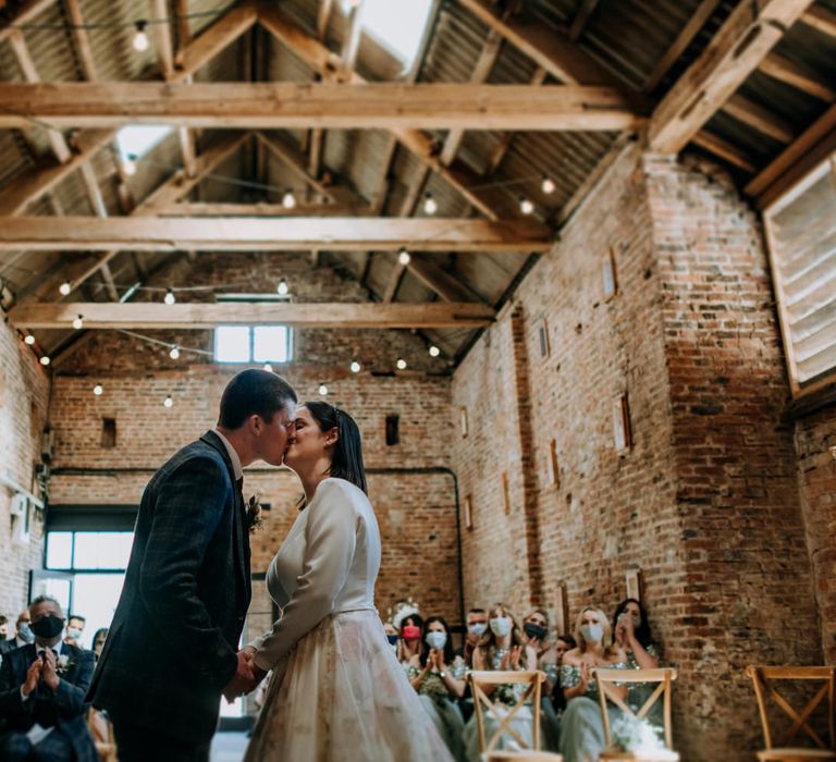 Bride and groom kissing at the altar of The Barns, East Yorkshire with the bride in a long sleeve wedding dress