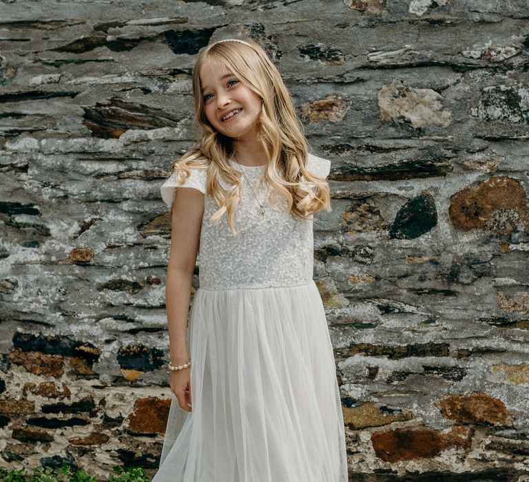 Bridesmaid stands in front of wall whilst wearing sequinned dress and hair in loose curls