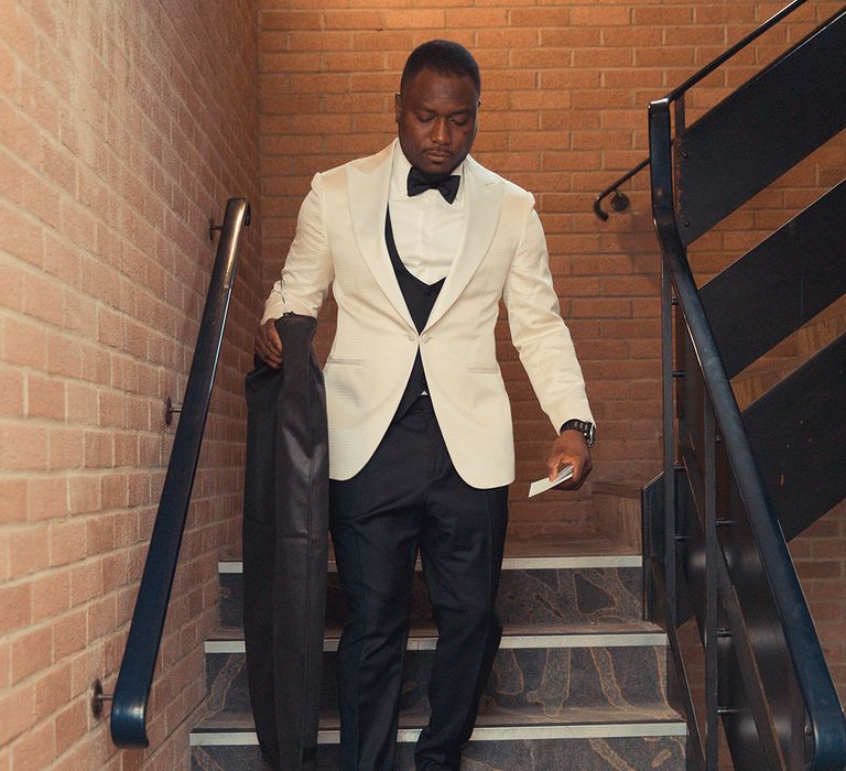 Groom walks down the stairs wearing a white tuxedo 