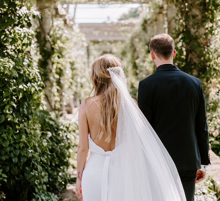 Bride & groom walk together as brides veil blows in the wind