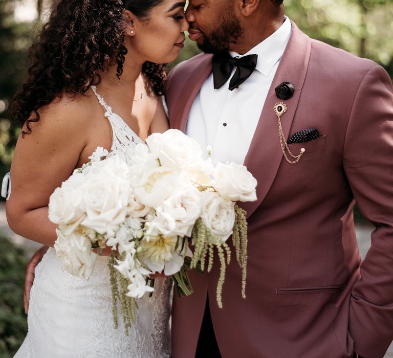 Groom kisses the forehead of his bride as she holds white floral bouquet