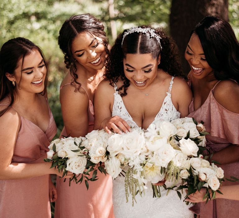 Black bride stands with her bridesmaids in blush pink gowns as they hold white floral bouquets in classic style