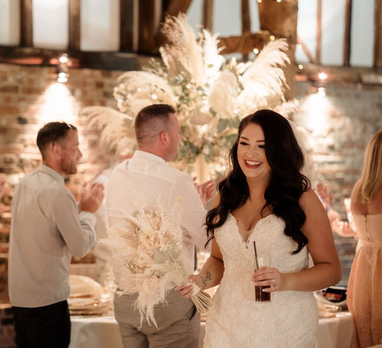 Beautiful bride walking through the barn wedding reception holding a dried flower wedding bouquet 