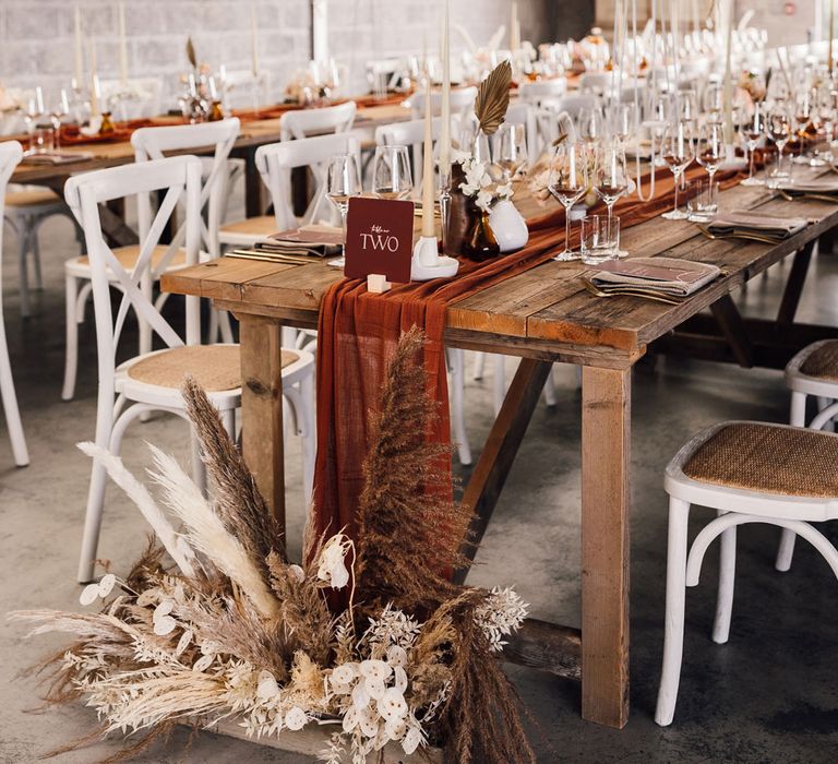 Interior of boho wedding reception with long wooden tables, pampas grass and boho decor with hanging chandelier and drapery