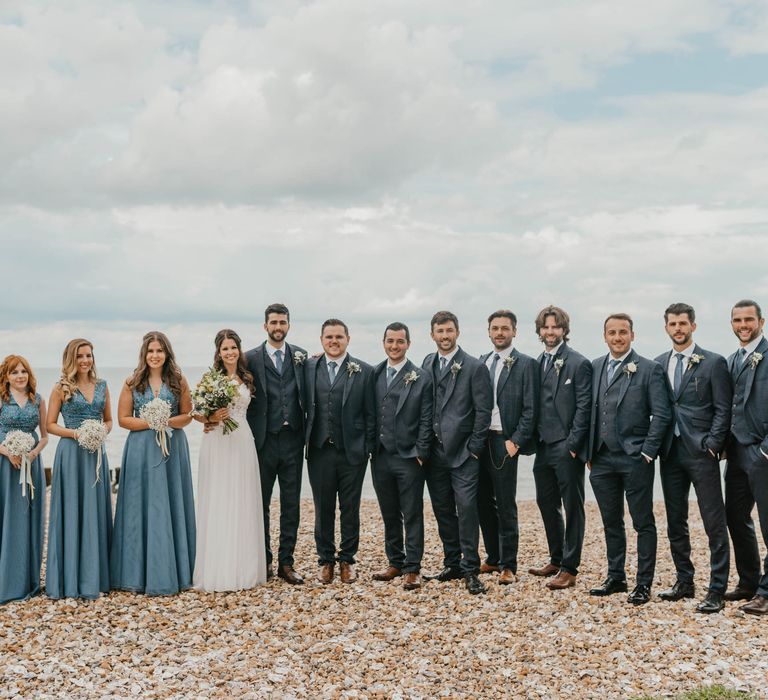 Bride & groom stand with their groomsmen and bridesmaids on the beach