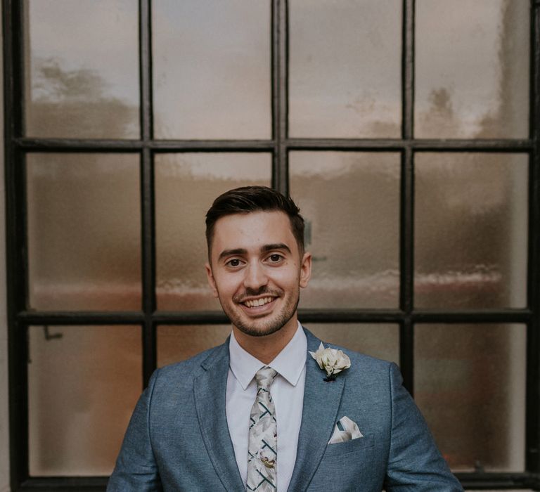 Groom in a mid-grey wedding suit doing up his jacket button at London wedding 