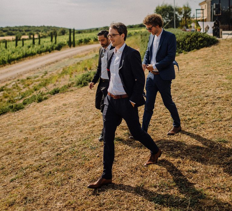 Groom walks with his groomsmen across golden fields in Croatia on his wedding day