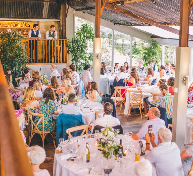 Wedding guests gather in rustic reception venue  | Story + Colour