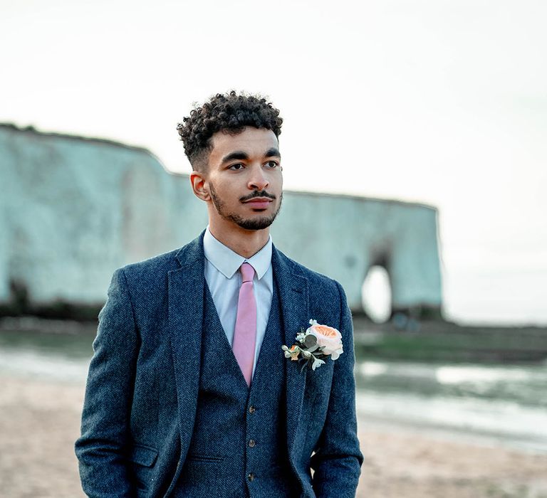 Groom in a blue wool three-piece suit with pink tie and rose buttonhole 