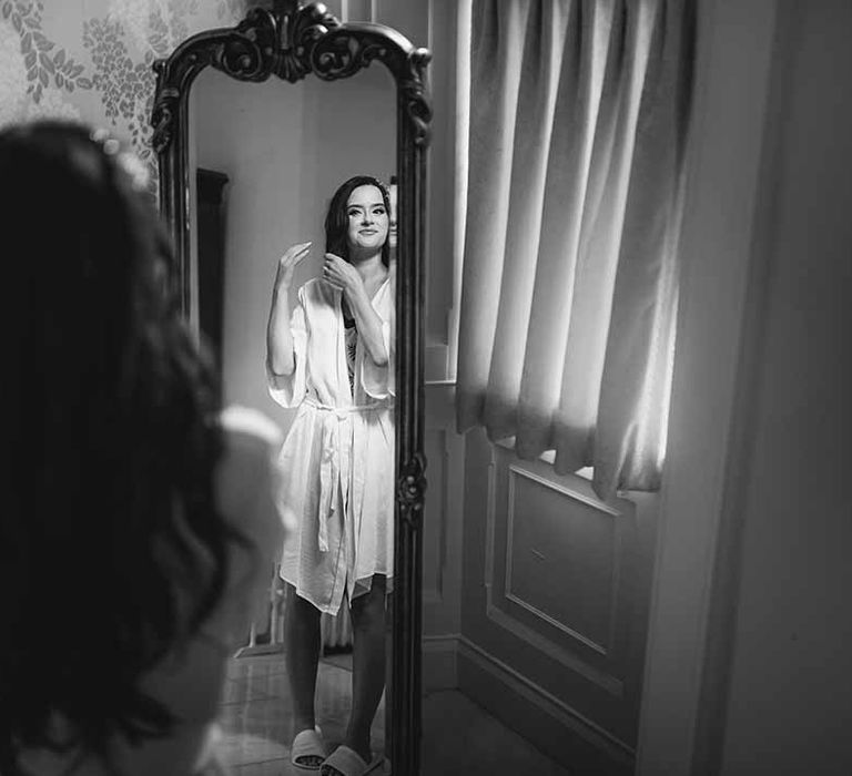 Bride gets ready in manor house room in her silk bridal robe 