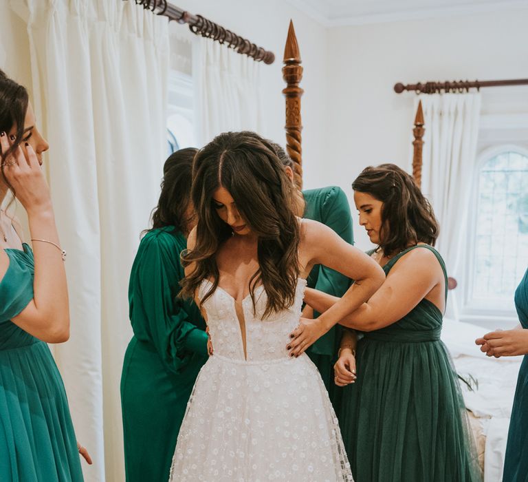 Bride in cami strap Pronovias wedding dress with mesh applique skirt has back of her dress tied by bridesmaids in mixed green bridesmaid dresses before Notley Abbey wedding