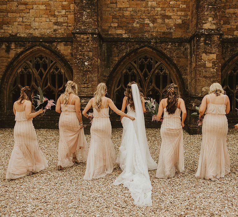 Bride stands with her bridesmaids who wear sparkly bridesmaid dresses 