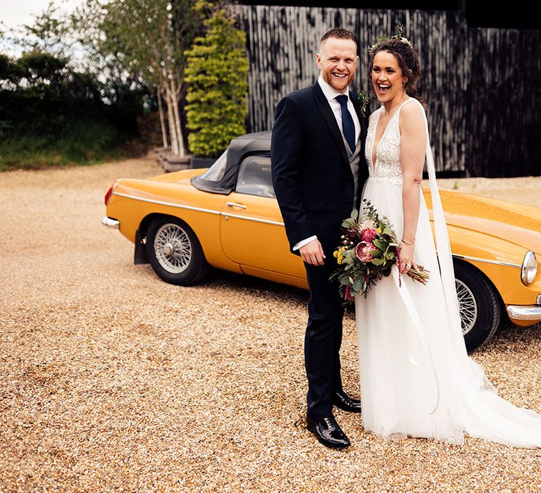 Bride and groom stand in front of vintage wedding car