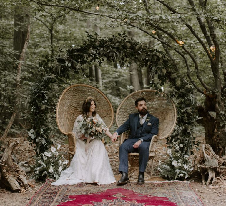 Bride & groom hold hands whilst sitting in sweetheart chairs