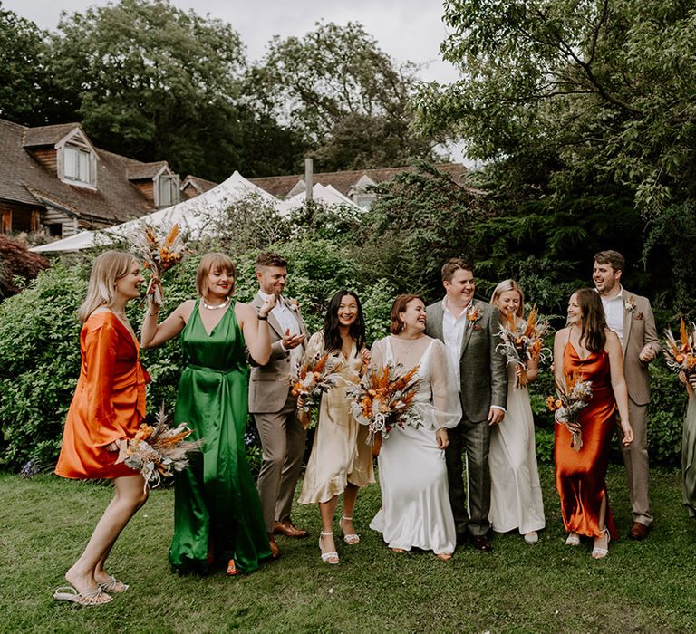 Fun wedding party photography with orange and green satin bridesmaid dresses and groomsmen in stone suits