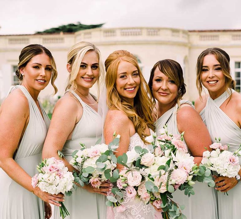 Bride and her bridesmaids hold white floral bouquets complete with green foliage